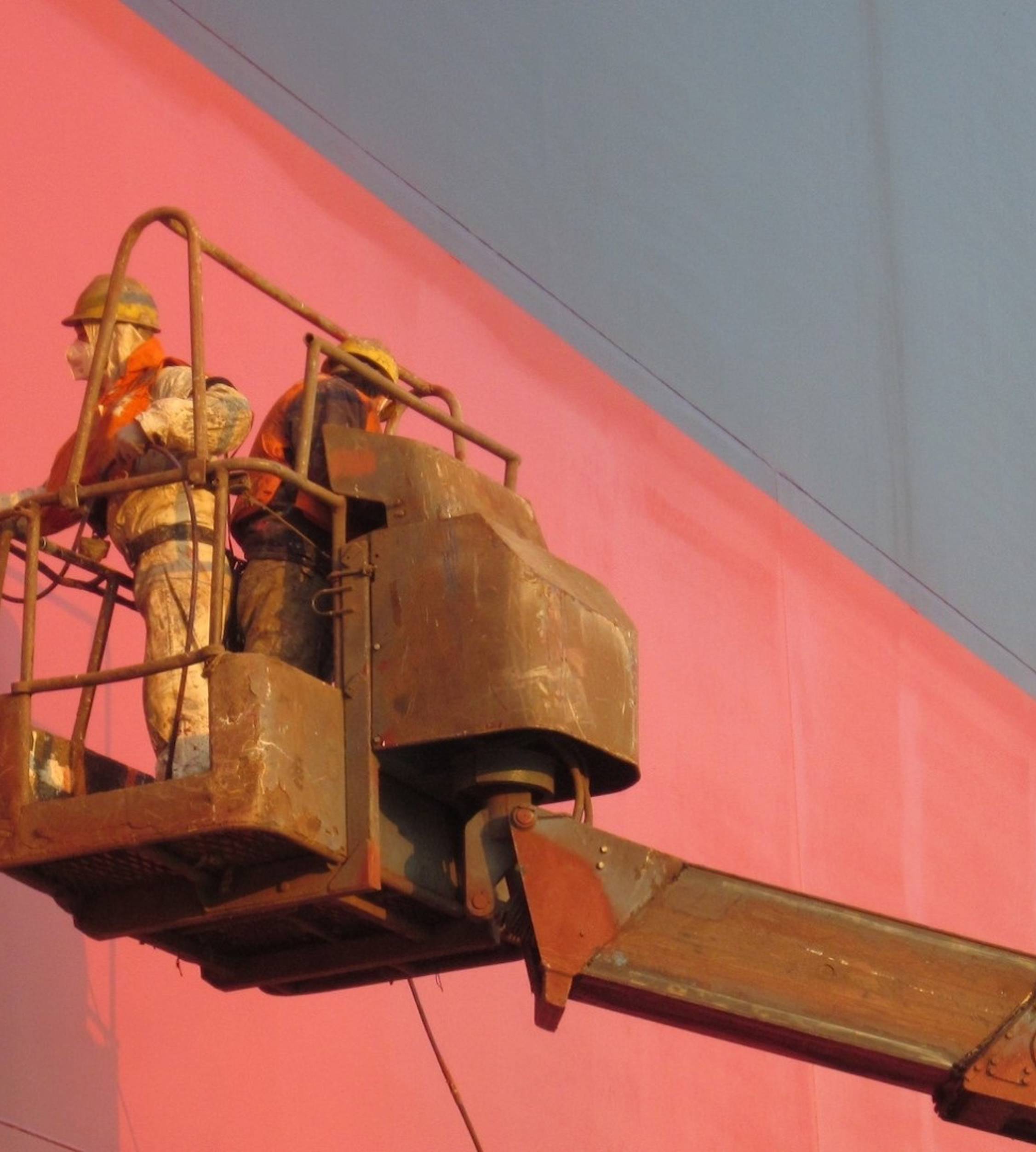 Two applicators spray painting red ship hull