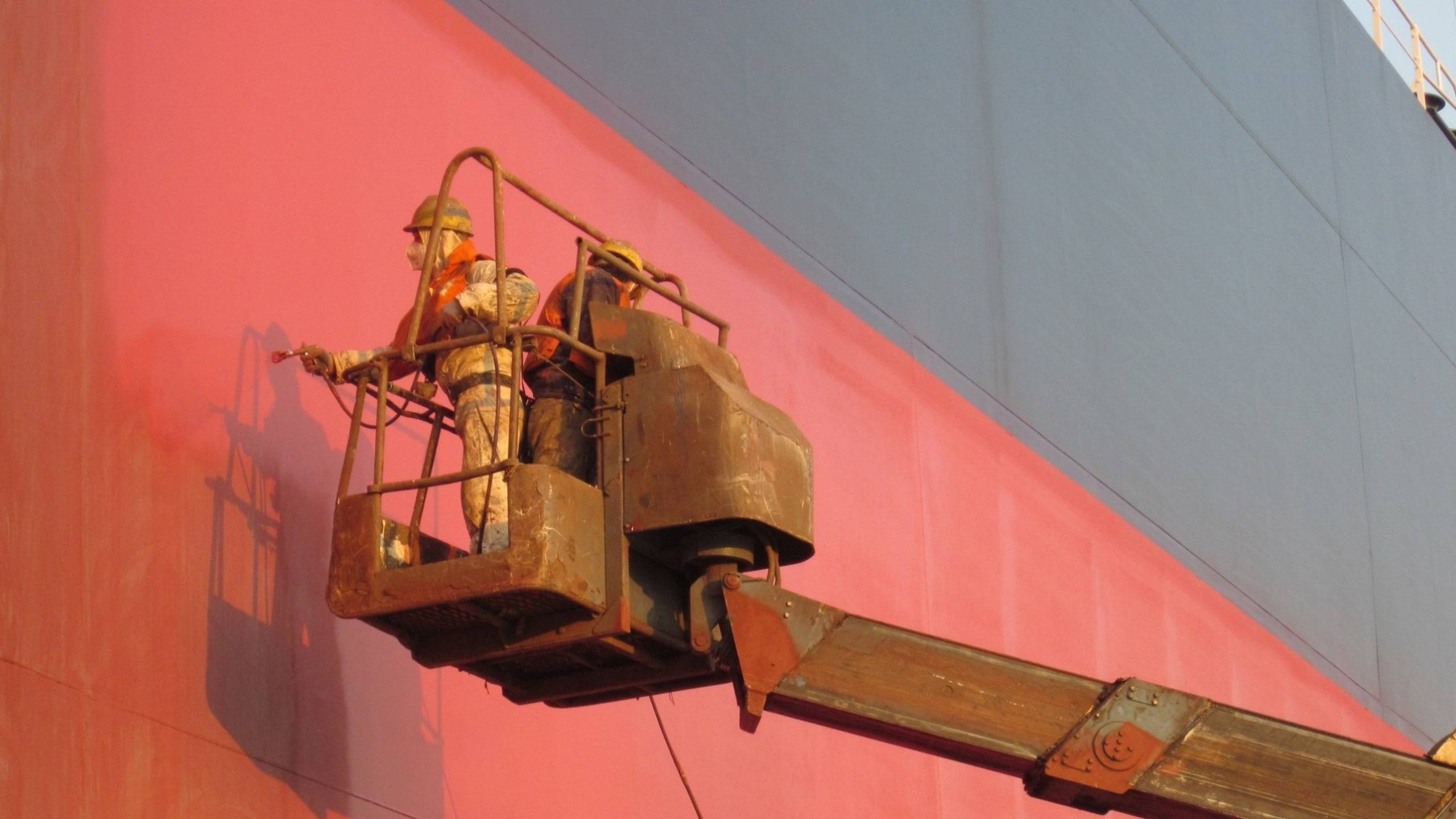 Two applicators spray painting red ship hull